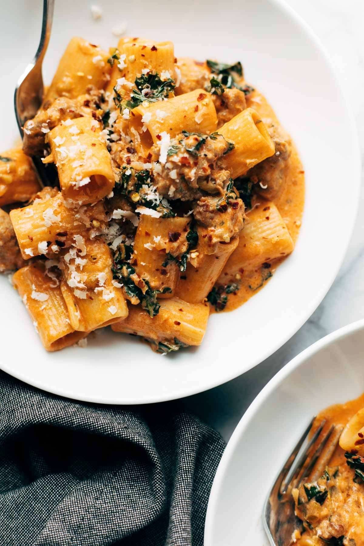 Rigatoni with sausage and kale in a bowl with a fork.