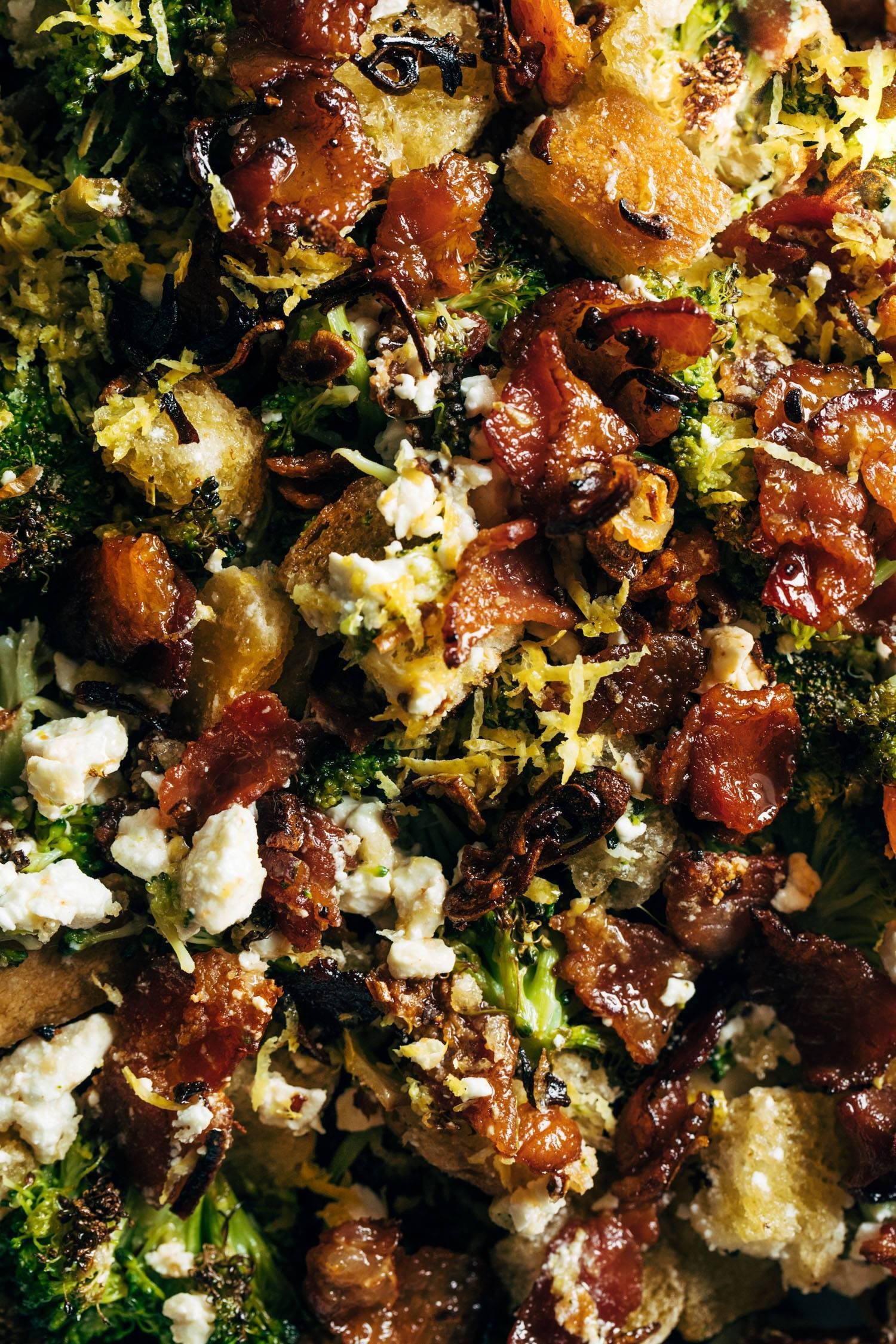 Close-up of roasted broccoli, bacon, lemon zest, sourdough croutons, and feta cheese.